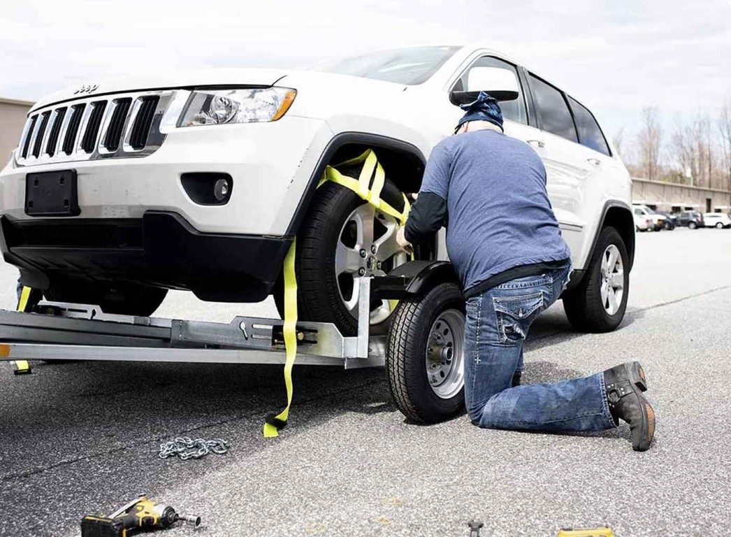 Technician performing a flat tire change on a Jeep Grand Cherokee in West Babylon, NY