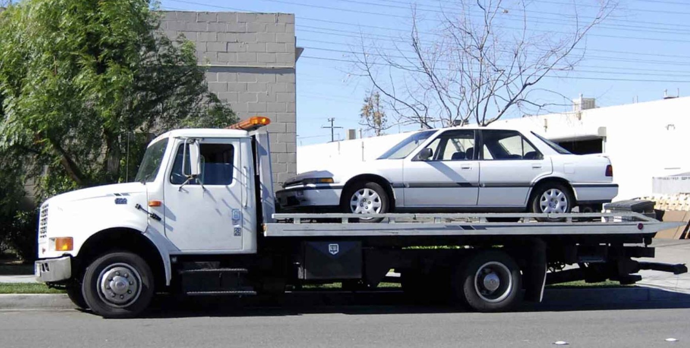 White flatbed tow truck transporting a sedan in West Babylon, NY